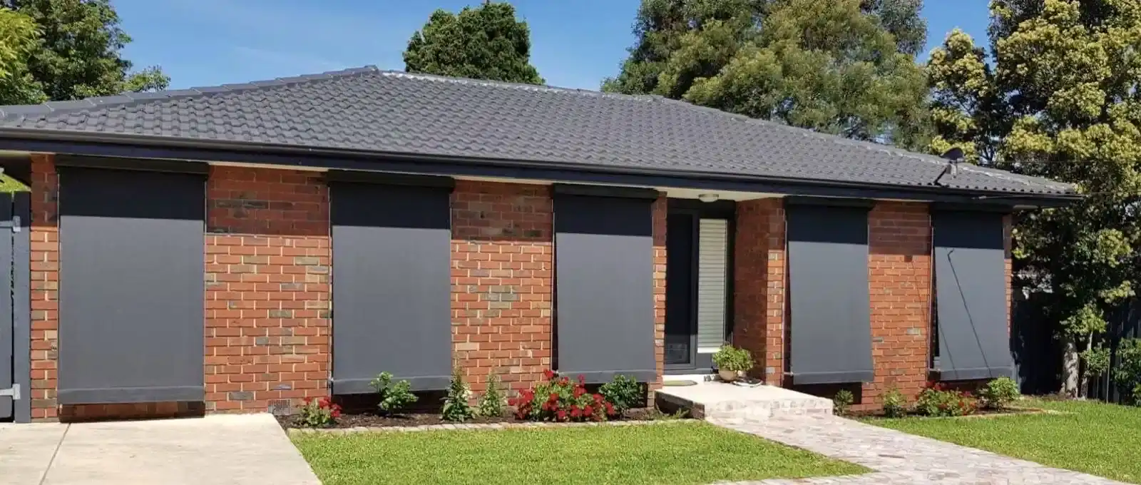 Charcoal outdoor blinds lowered across multiple windows on the brick exterior of a house.