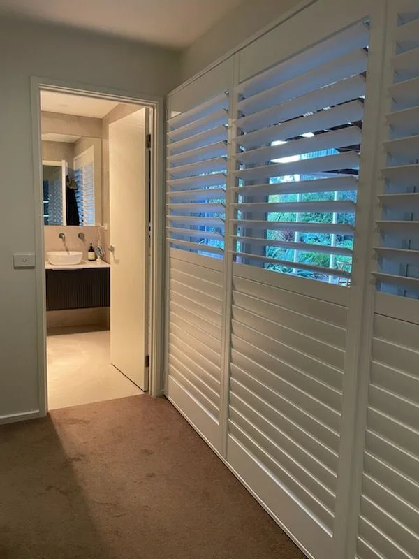 White plantation shutters in a hallway with a view through to an ensuite bathroom.